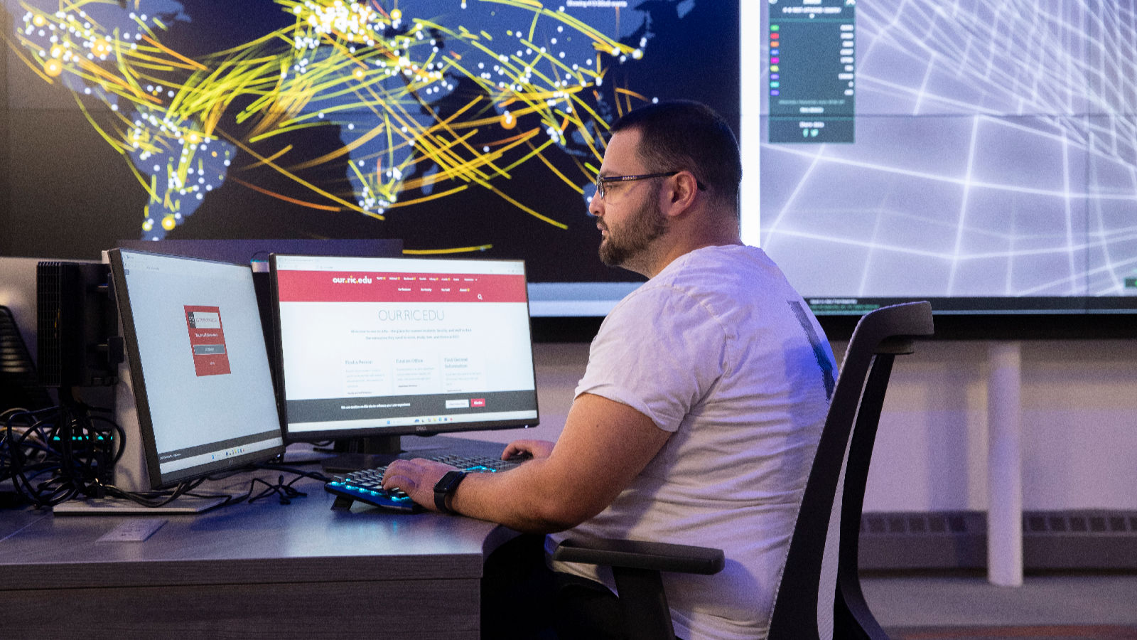 A man sits at a computer with cybersecurity graphics in the background.